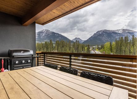 Mountain view balcony with wood table and grill.